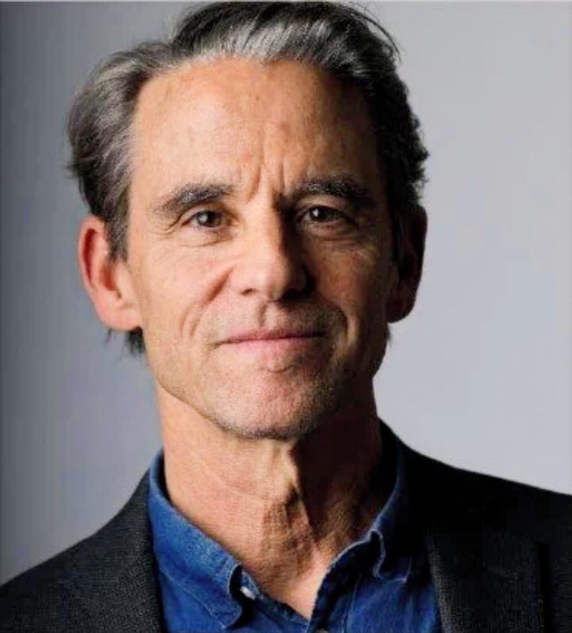 A color photo of Andre Carothers, looking at the camera, smiling. He has short length hair, and is wearing a blue shirt with a black suit jacket.