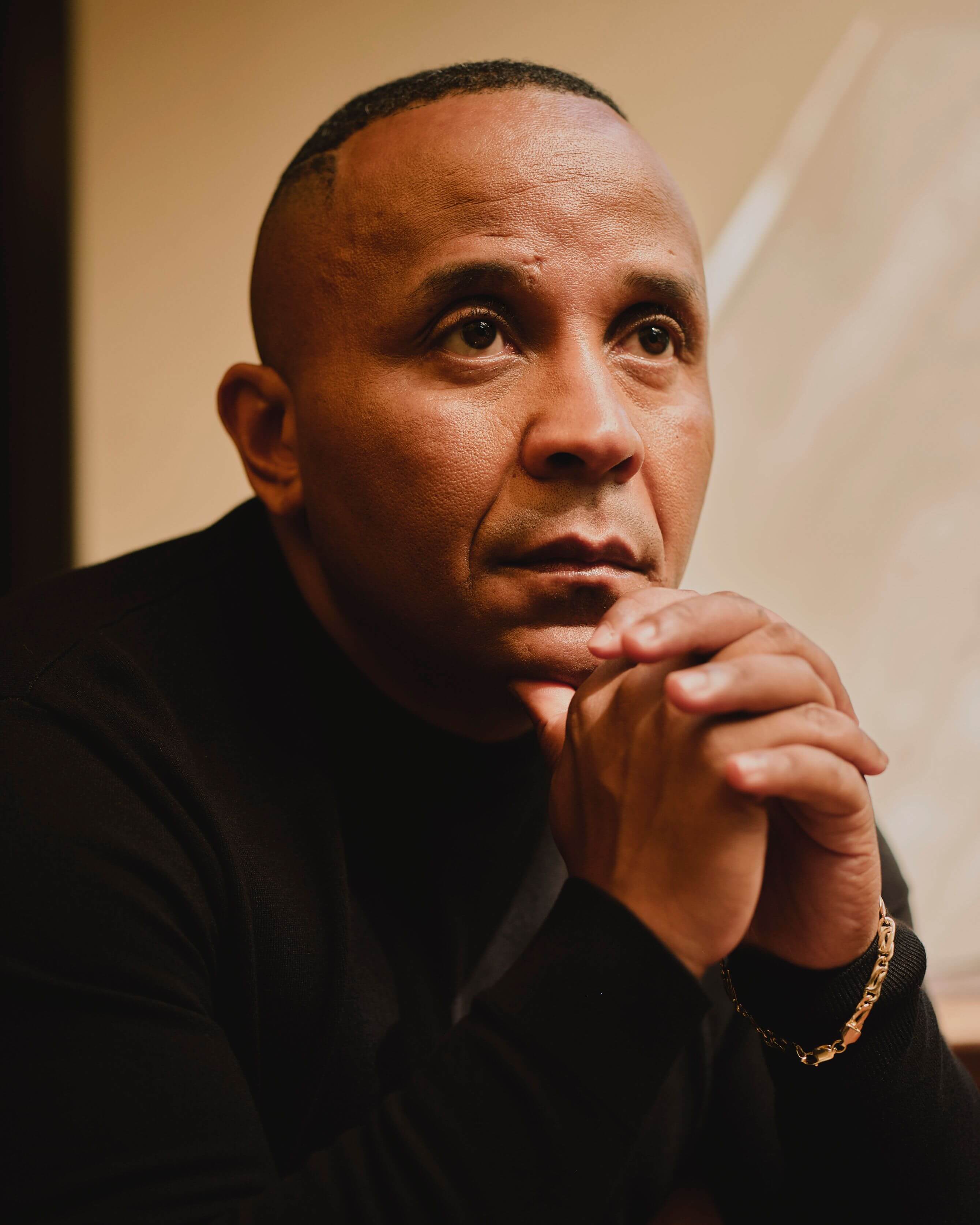 Photo of Rashad Robinson holding his hands together. Rashad is wearing a black suit with a gold bracelet and looking off into the distance
